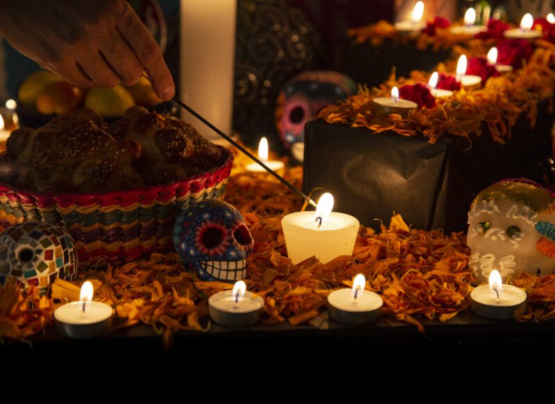 Hand holding incense stick over "ofrenda" for the Day of the Dead in Puebla, Pue., Mexico, as an example of holidays around the world