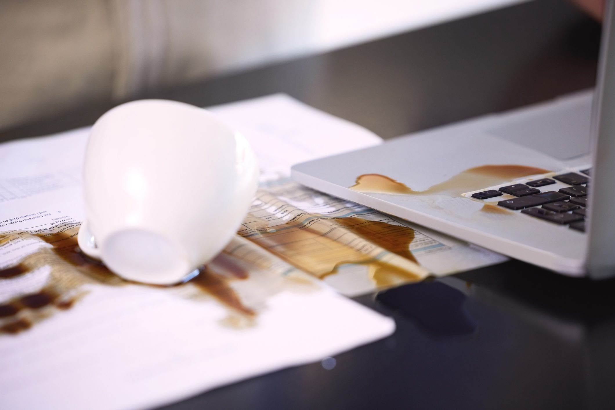 Dizüstü bilgisayar ve kağıtlar ve dökülen bir fincan kahve ile masa