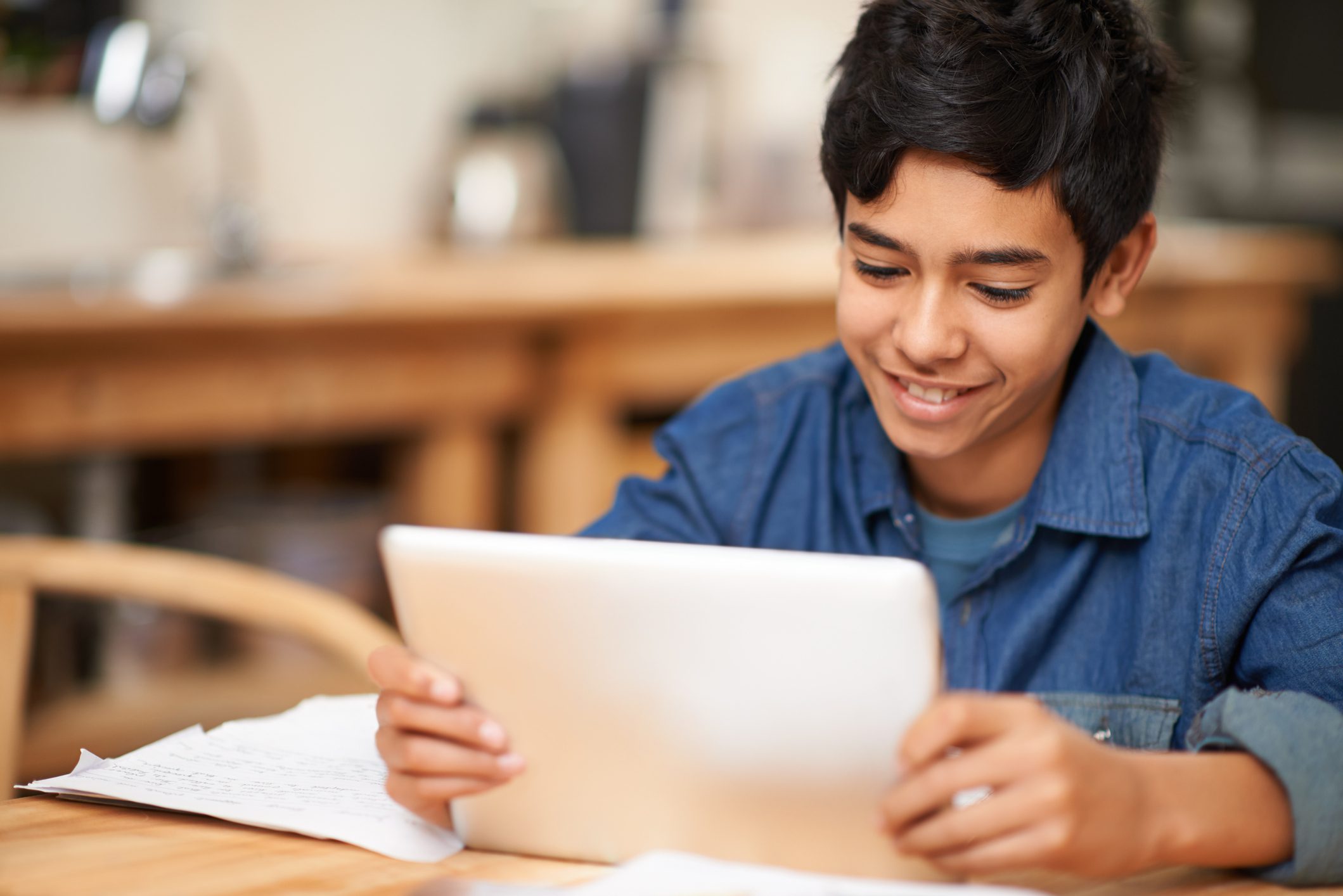 Shot of a young teenage boy using a digital tablet while doing his homework