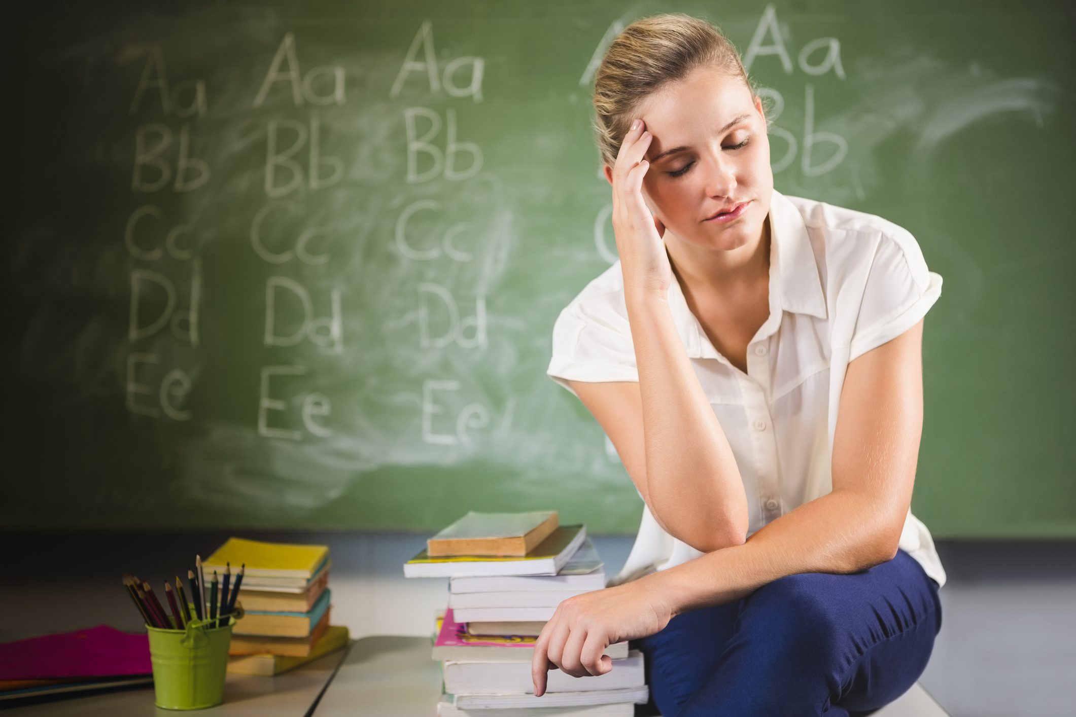 ensed school teacher sitting with hand on forehead in classroom at school