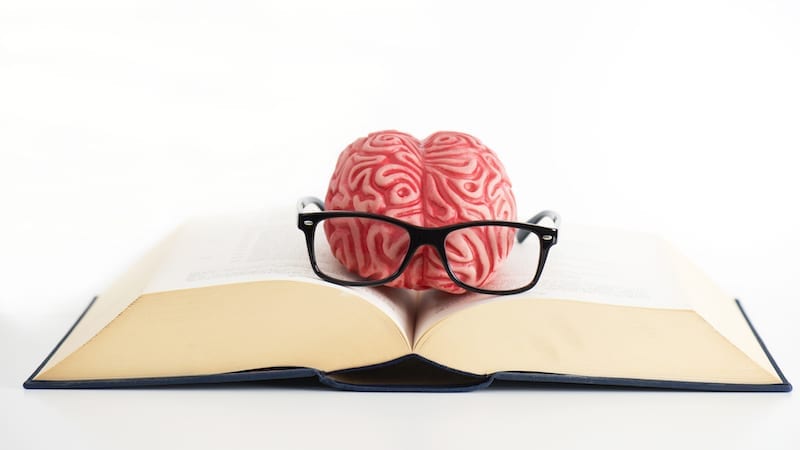 Brain with eyeglasses on top of a open book.
