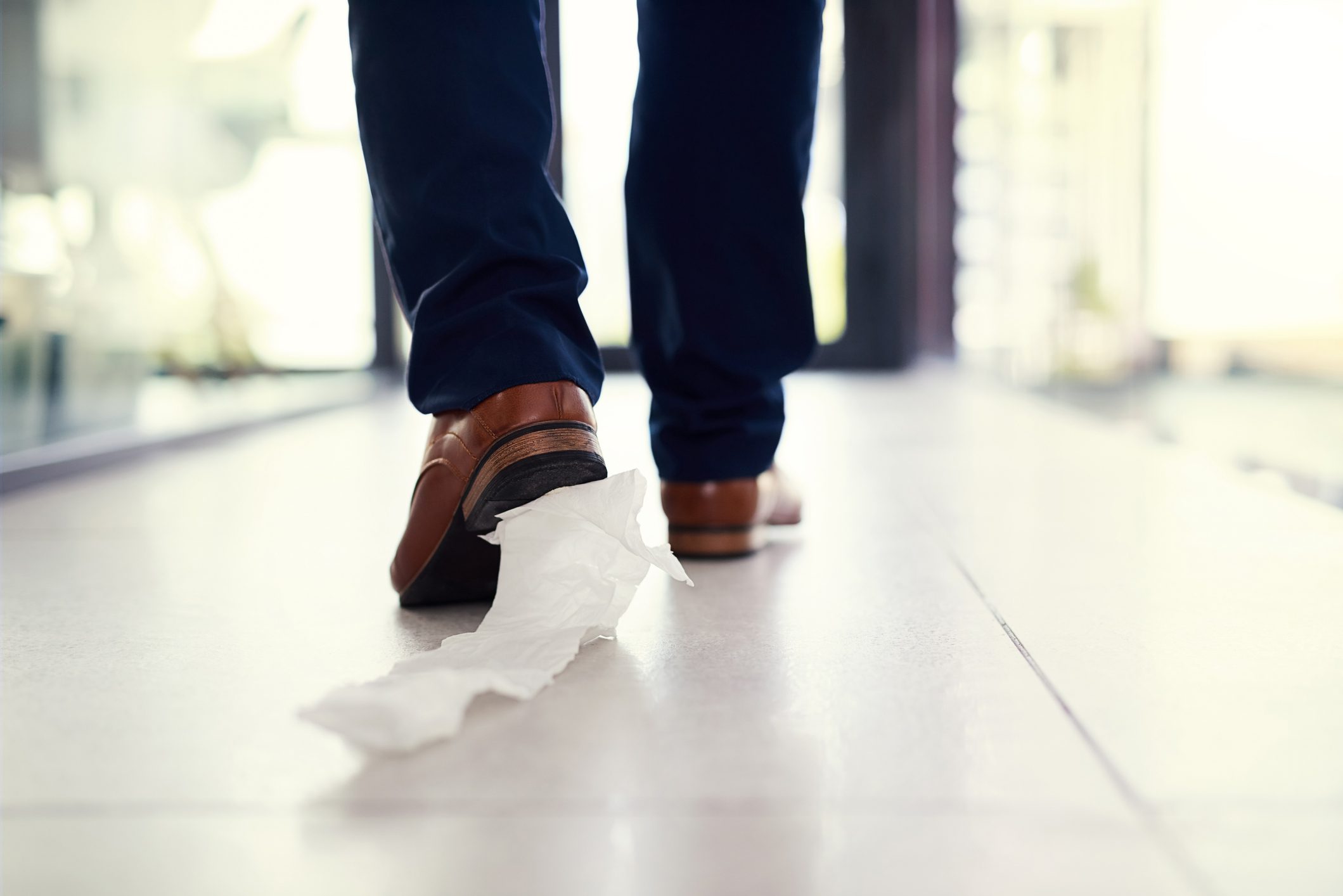 Ayakkabısına tuvalet kağıdı yapıştırılmış bir ofiste yürüyen bir iş adamının yakın plan fotoğrafı.