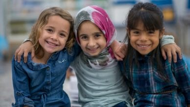 three young girls sit happily with their arms around one another
