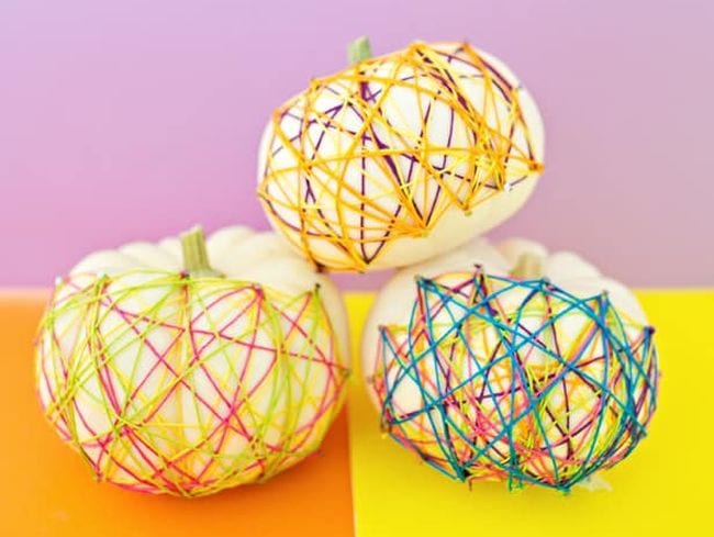 White pumpkins decorated with colorful string art are used in Halloween activities like this one. 