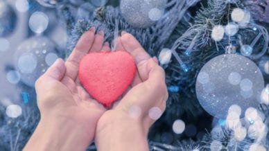 Female hands hold heart on Christmas tree.