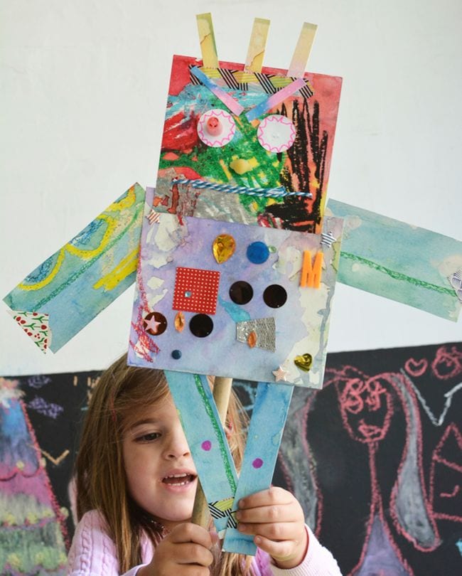 Kindergarten child holding a mixed media paper robot with buttons, fabric, and other materials (Kindergarten Art)