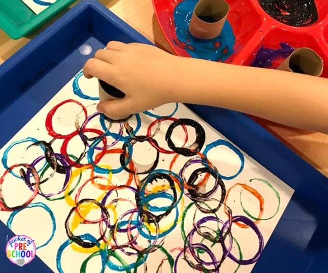 Kindergarten art student's hand using a toilet paper tube dipped in paint to make colorful circles