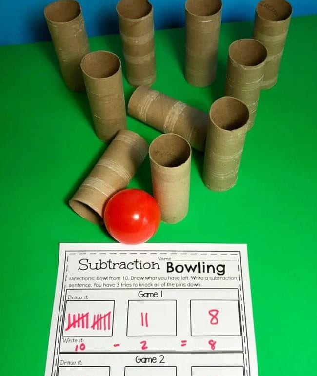 Tubos de papel higiénico montados como pinos de bowling, com uma bola vermelha e folha de trabalho chamada Subtracção Bowling