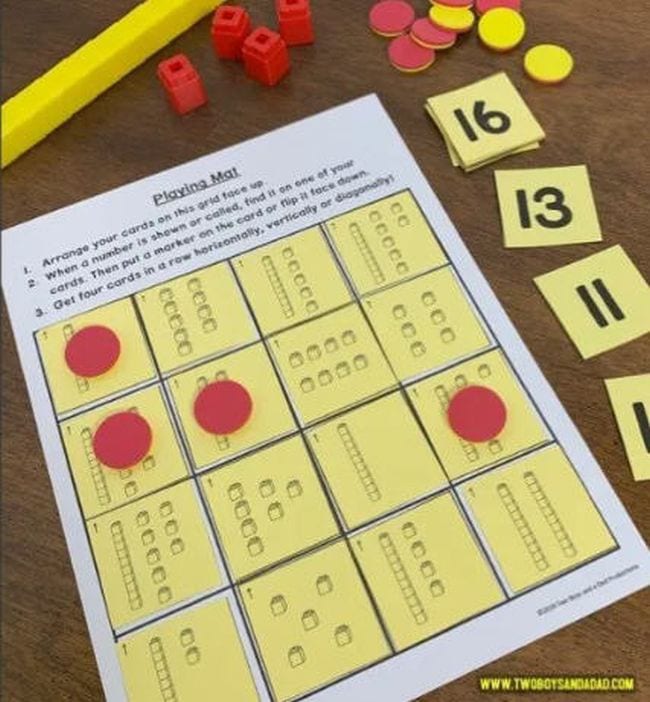 Carte divisée en une grille, avec des cubes mathématiques montrant différents chiffres sur chacun, avec des cartes de chiffres et des marqueurs rouges