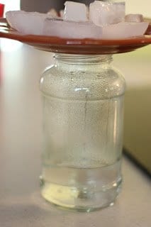 glass jar with a couple of inches of water in it topped by a plate filled with ice cubes