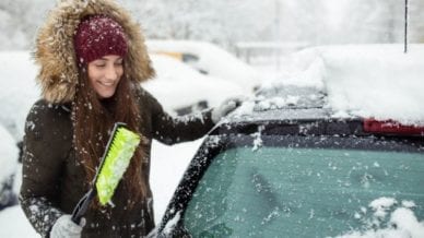 A woman scrapping the snow off her car window.