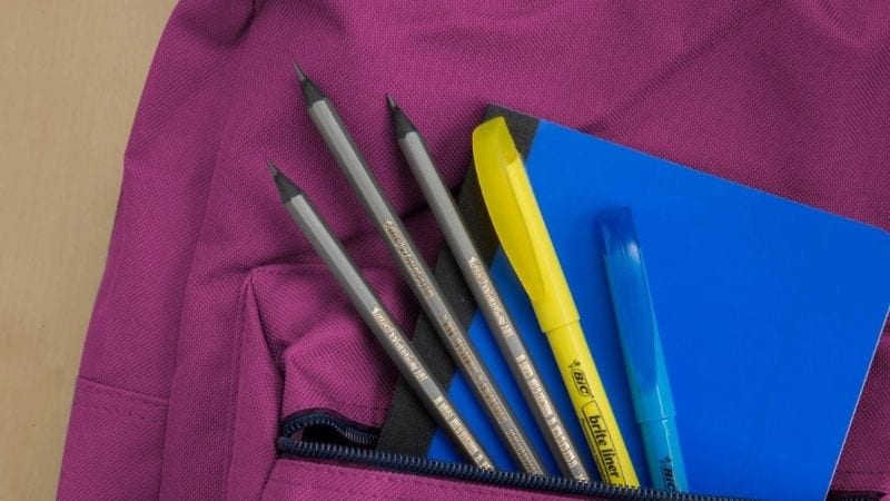 A purple background with the zipper open full of pens, a notebook, and highlighter.