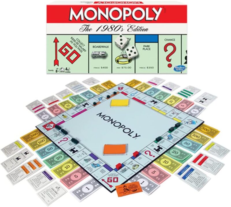 A white game box says Monopoly in large letters. A game board is shown with fake money spread all around it (educational board games)
