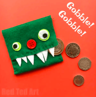 4 coins tumble from a change purse made from green felt folded in thirds, with a red button nose and googly eyes and white fangs made from felt., as an example of summer crafts for kids