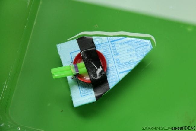 Toy boat made from styrofoam, bottle cap, and straws, floating on water