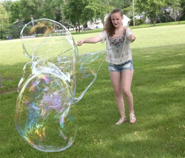 Student creating an enormous soap bubble with string on sticks (Outdoor Science)