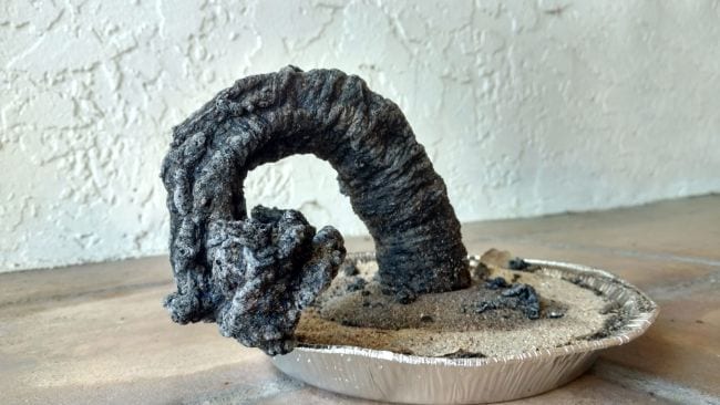 Large carbon snake growing out of an aluminum pie plate of sand