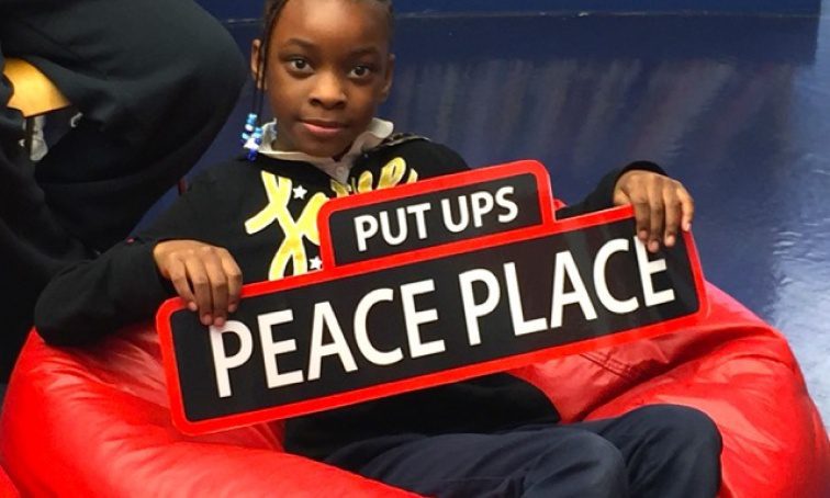 young student sitting in a bean bag chair holding a sign that says PEACE PLACE