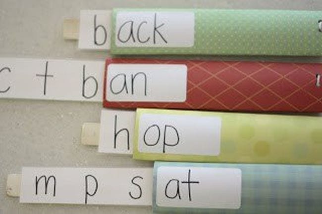 Paint stirring sticks labeled with letters, tucked into paper sleeves with word endings on them