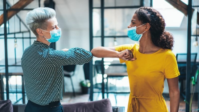 Two female colleagues at work with masks on giving each other an elbow bump