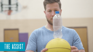 A P.E. teacher holding a basketball while balancing an empty water bottle on top.