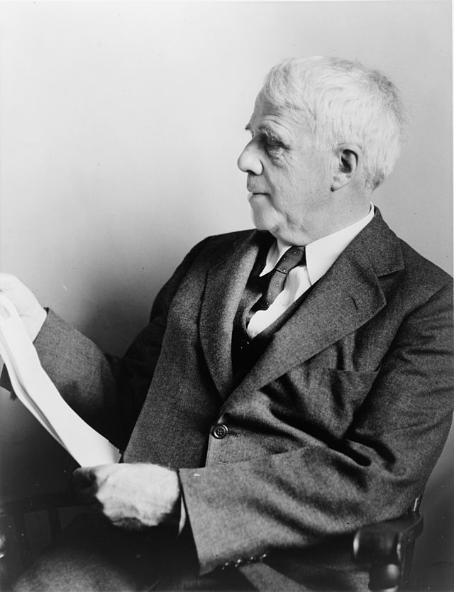 Black and white photograph of Robert Frost reading a manuscript.