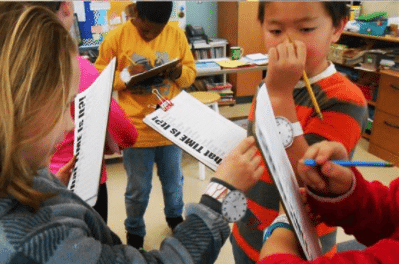 Students holding clipboards and look at the time on each other's paper watches (Telling Time)