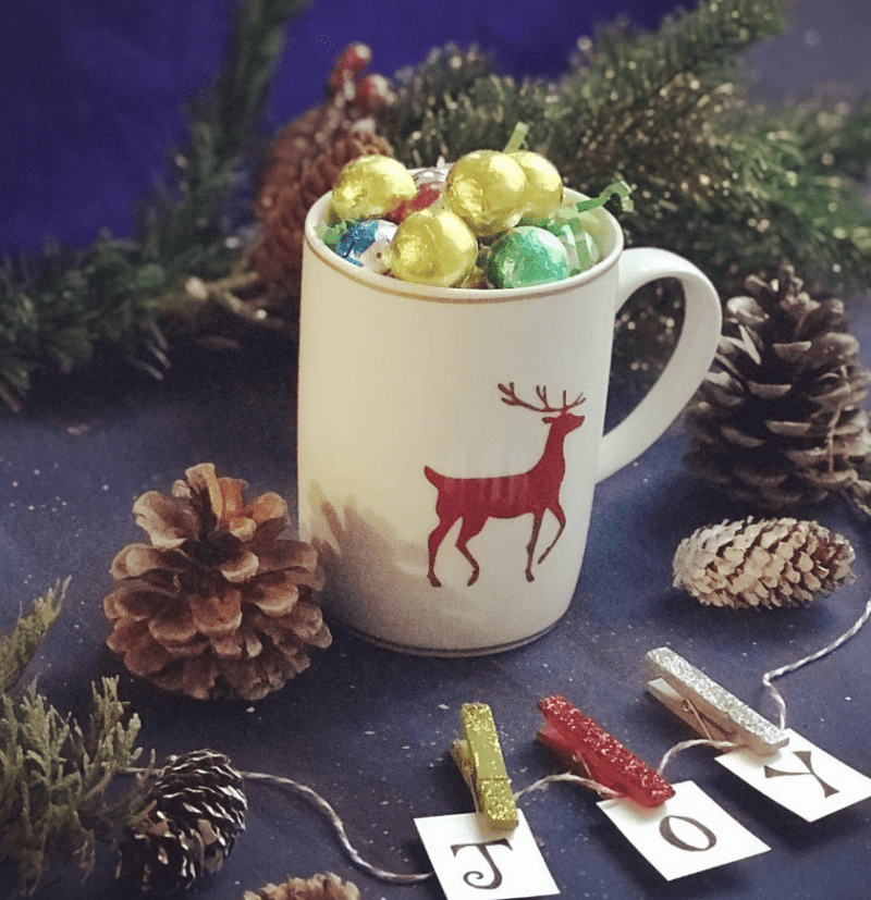 Mug with reindeer design on it filled with colorful chocolates