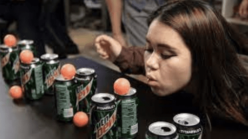 Girl blowing ping pong ball off of soda can