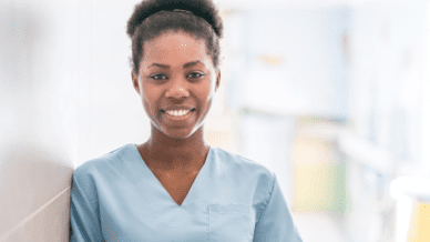 A young adult African American woman smiling while wearing light blue scrubs.