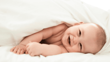 A baby smiling while wrapped in a white blanket.