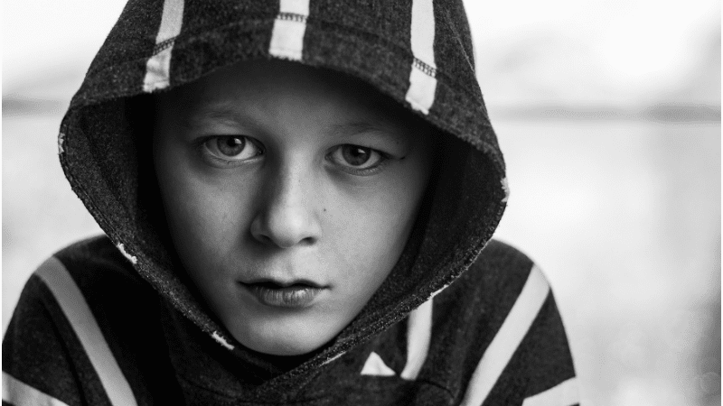 young boy wearing a hooded sweatshirt looks sad