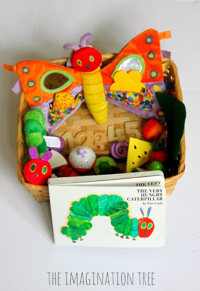 A basket filled with a plush caterpillar and items of toy food with the book The Very Hungry Caterpillar in front 