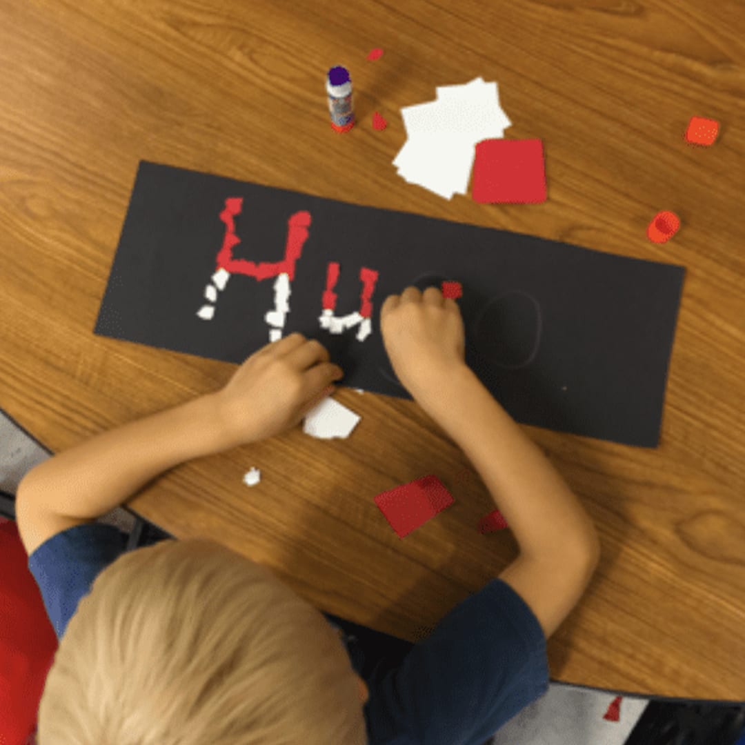 A student sitting at a desk making letters out of shapes inspired by Pokemon having the best day ever at school.