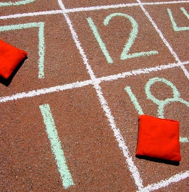 squares drawn on concrete with numbers inside, red bean bags in two of the squares