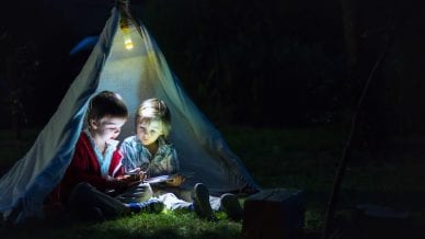 Cute little brothers, playing on tablet and telephone at night in campside, in the tent