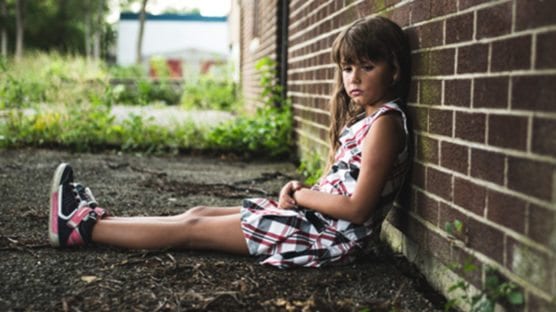 Young girl sitting against a brick wall outside of school needs a teacher to provide trauma-informed teaching strategies