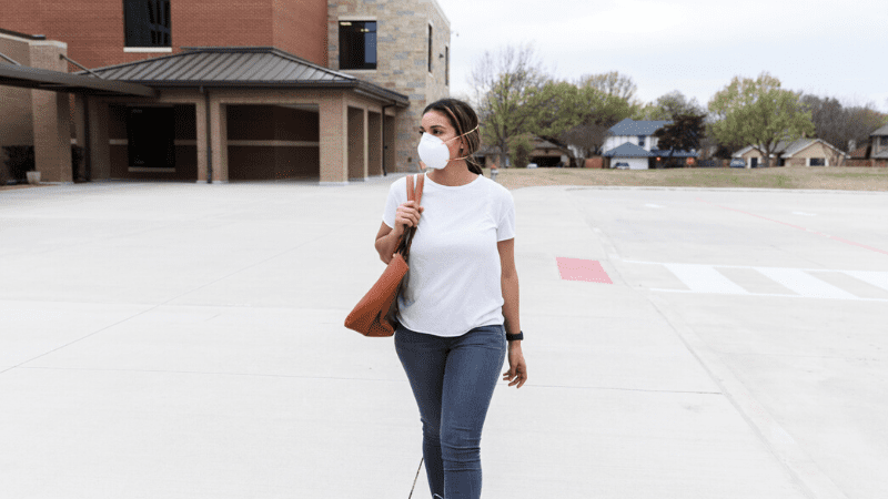 A young teacher wearing her N95 mask will walking on an empty school campus.