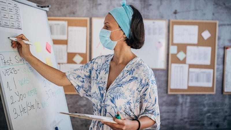 A teacher wearing a mask while writing her lesson on a whiteboard.