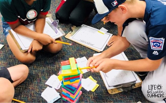 Students holding clipboards and using pencils to push wooden blocks out of a tower