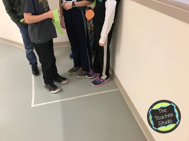 Students standing together in a taped-off square in the corner (Teaching Division)