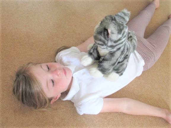 young girl laying on the carpet with a stuffed cat on her belly