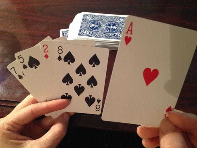 Student holding playing cards with a stack of cards on the table (Third Grade Math Games)