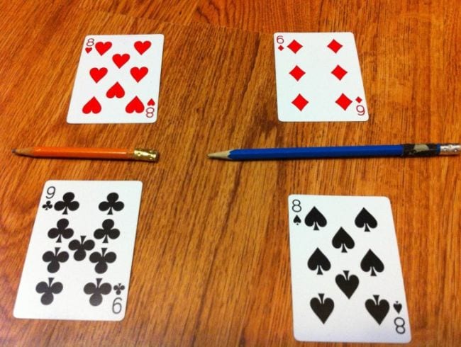 Four playing cards laid out as fractions with pencils as the lines (Third Grade Math Games)