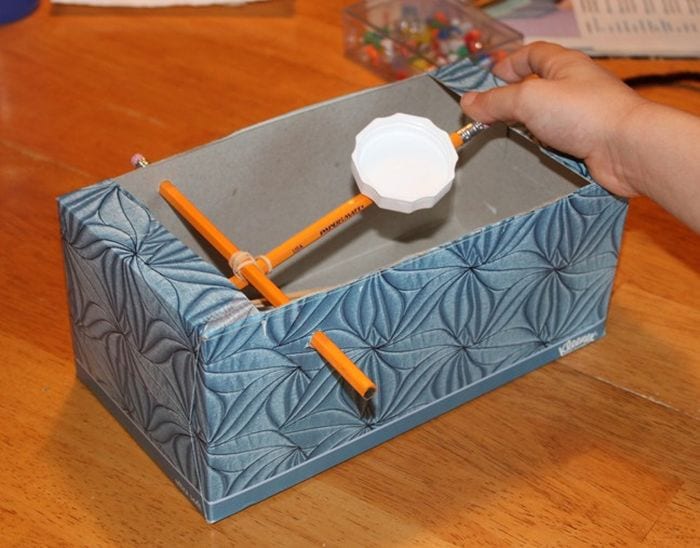 Third grade science student playing with a catapult made of a tissue box and pencils