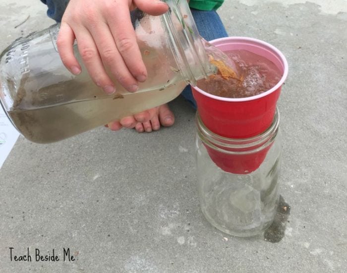 Child pouring dirty water into a cup propped over a jar