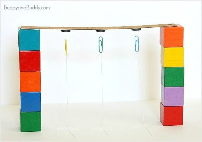 Bande de carton soutenue par des blocs colorés, avec des trombones suspendus à des aimants en dessous (Third Grade Science)