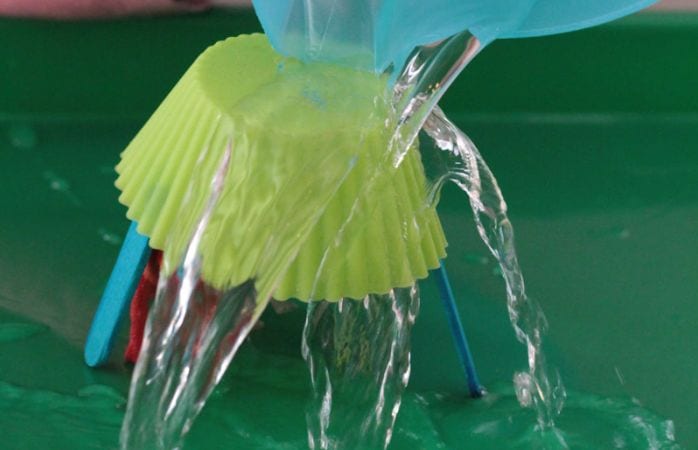 Cupcake wrapper balanced upside-down on wood craft sticks, with water being poured on top