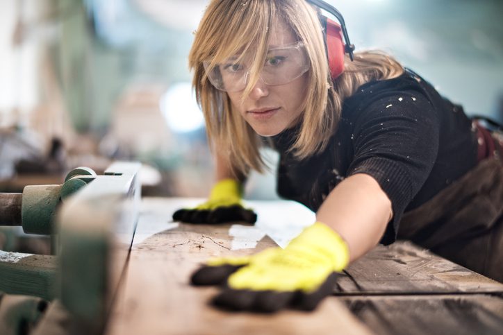 Blonde woman cutting a plank of wood with a saw