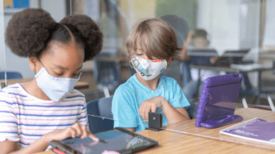 Two masked students working on iPads